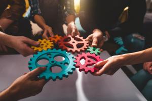 People standing in a circle, each holding a different colored gear