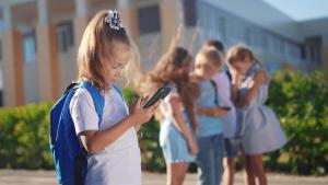 Young school girl on phone, standing separate from other students